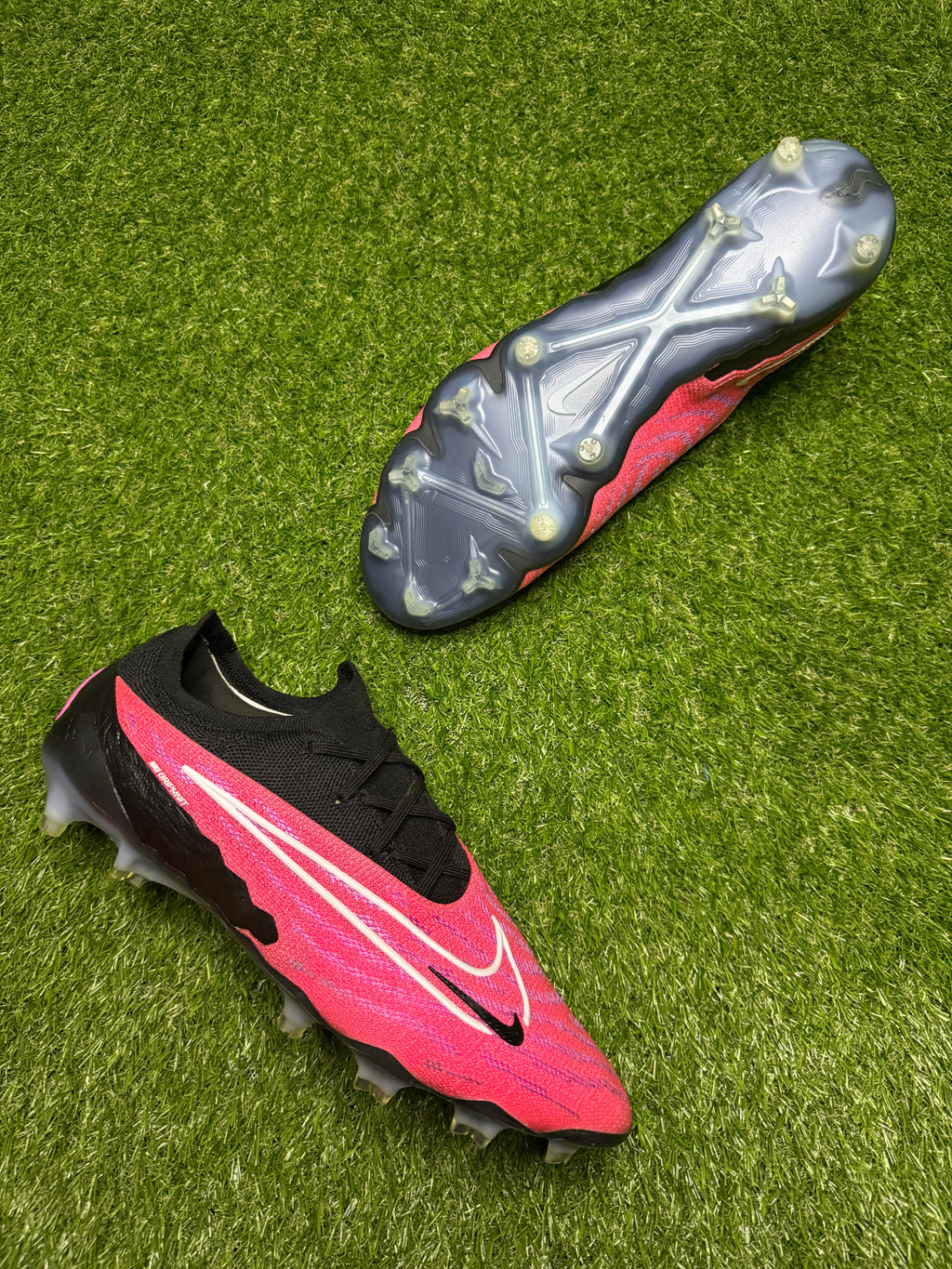 Two soccer cleats, one red and black and one gray and black, on a grassy surface.